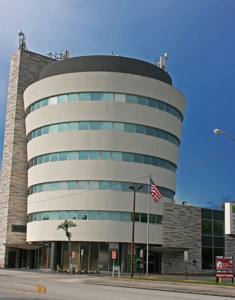 A curved, multi-storey commercial office building with banded windows and a United States flag flying outside.