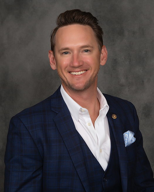 Ian Keith, President of Keith Insurance, smiling in a navy checked suit and open-collar white shirt.