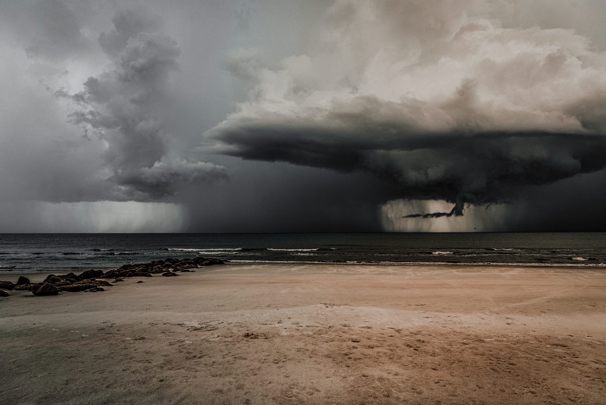 A dark rain squall sweeping in over the Gulf towards an empty stretch of pale sand beach.