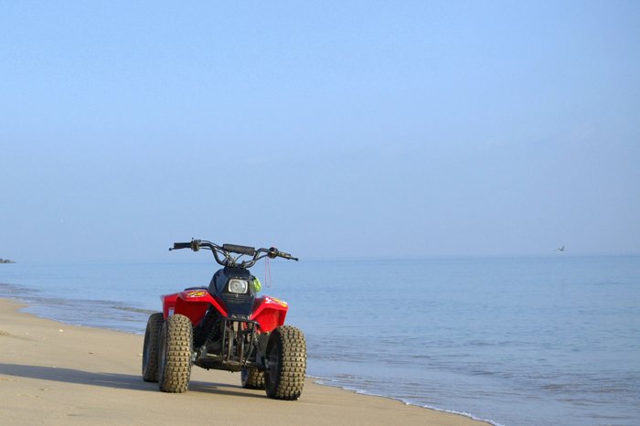 A red four-wheel ATV parked alone on wet sand at the edge of a calm sea on an empty beach.