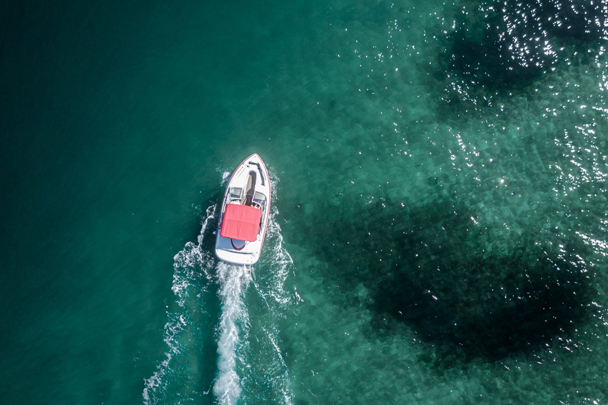 A small open motorboat cutting a white wake across clear turquoise water, seen from directly above.