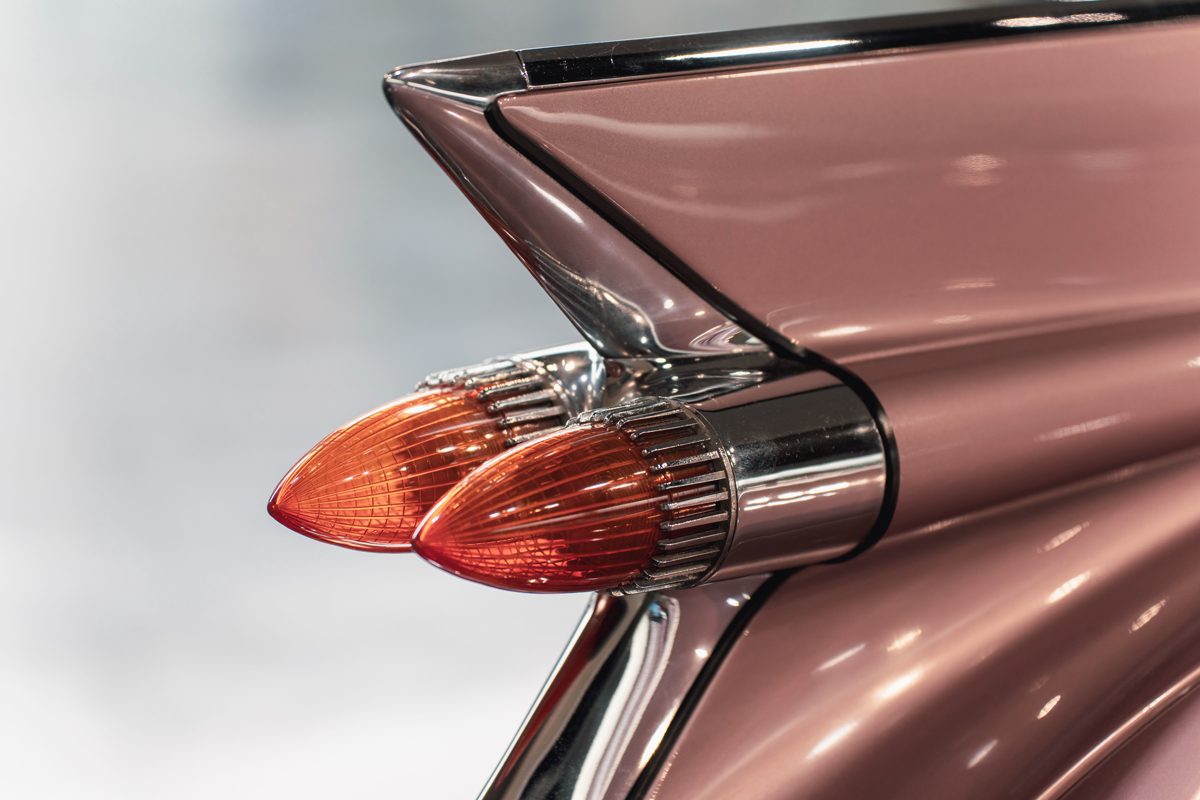 The chrome tail fin and twin bullet tail lights of a pale pink 1950s American convertible.